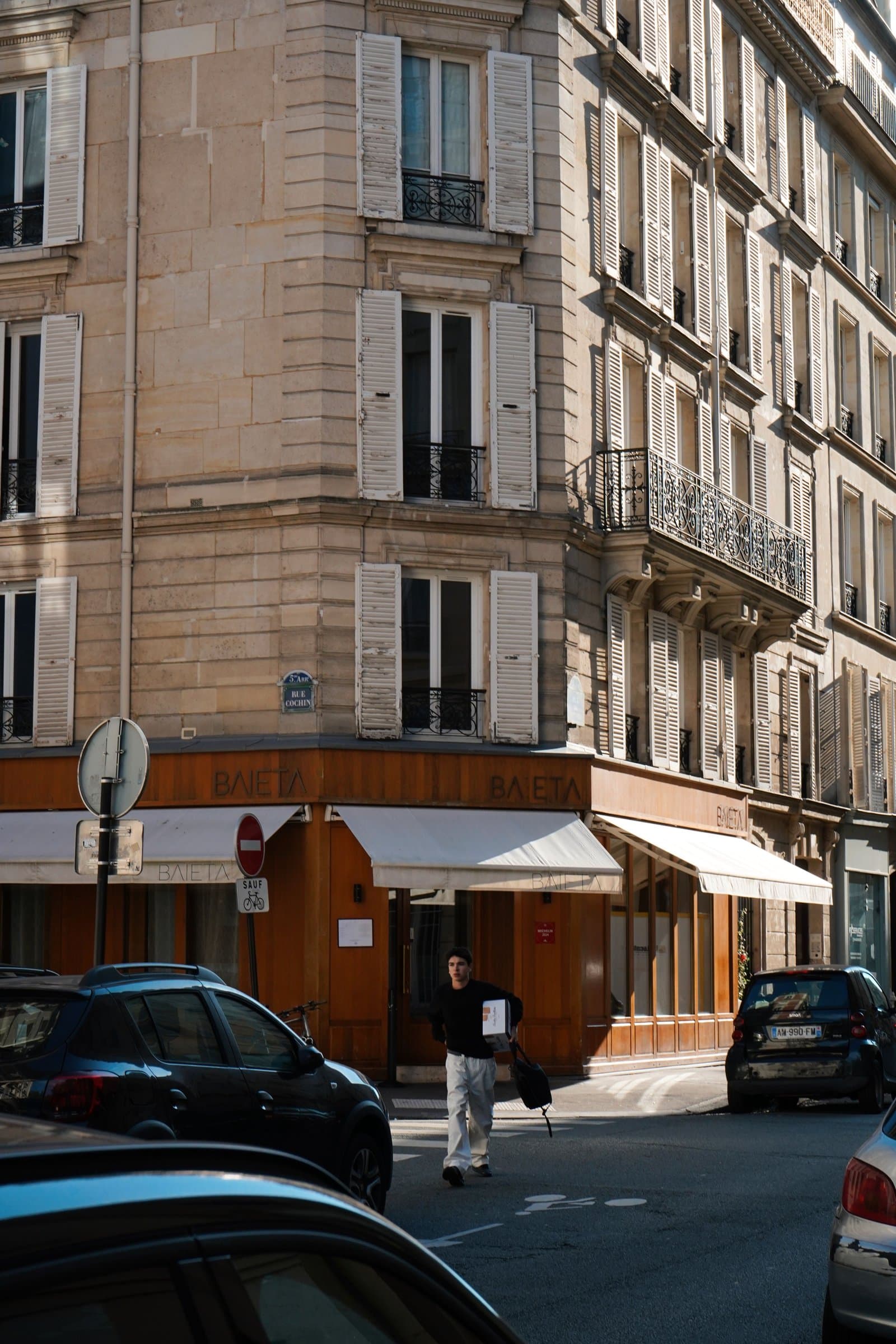 A quiet Parisian street corner with pale shuttered buildings and a restaurant awning below.