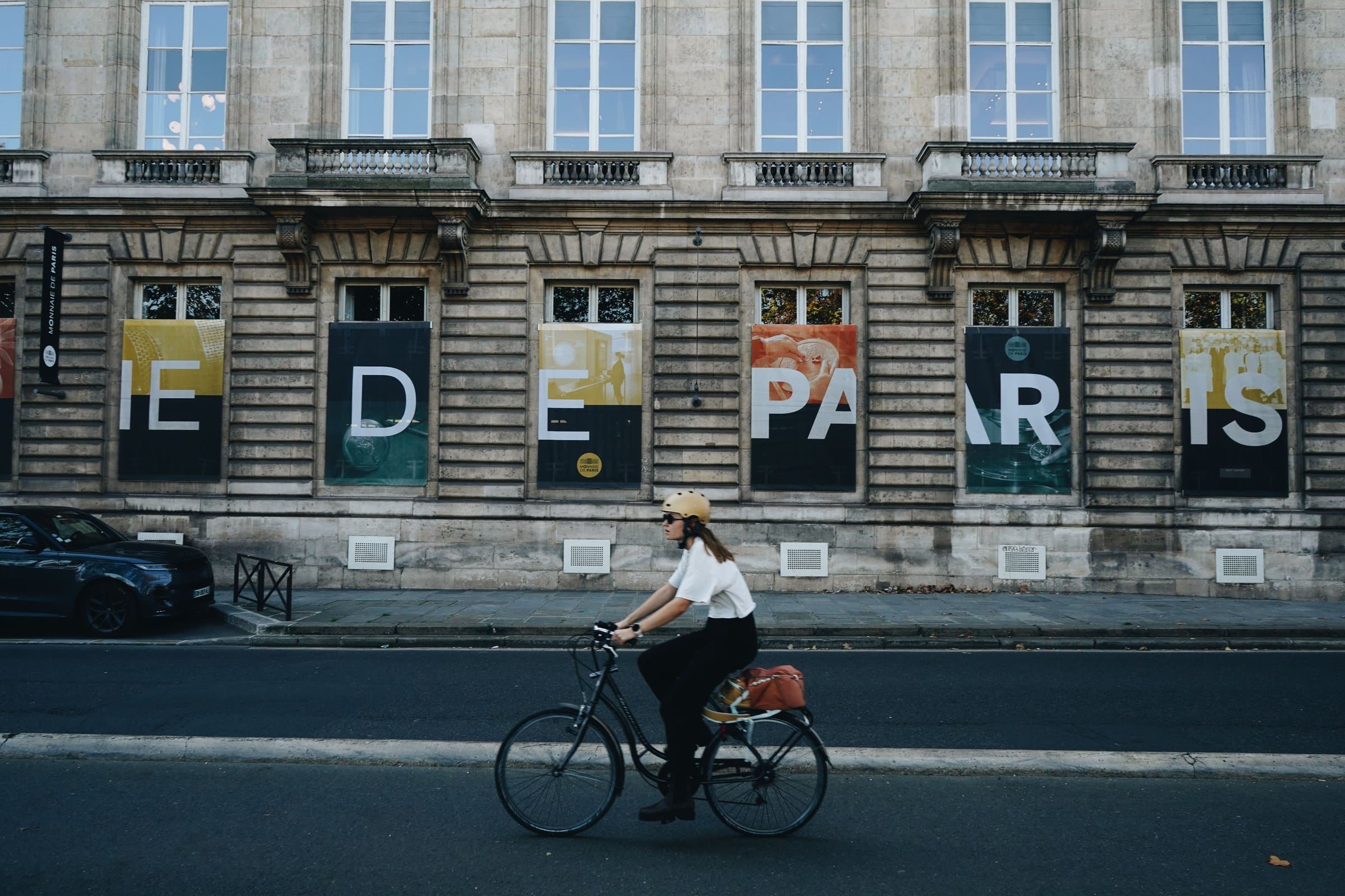 A cyclist passes the stone facade of the Monnaie de Paris, its windows dressed in banners.