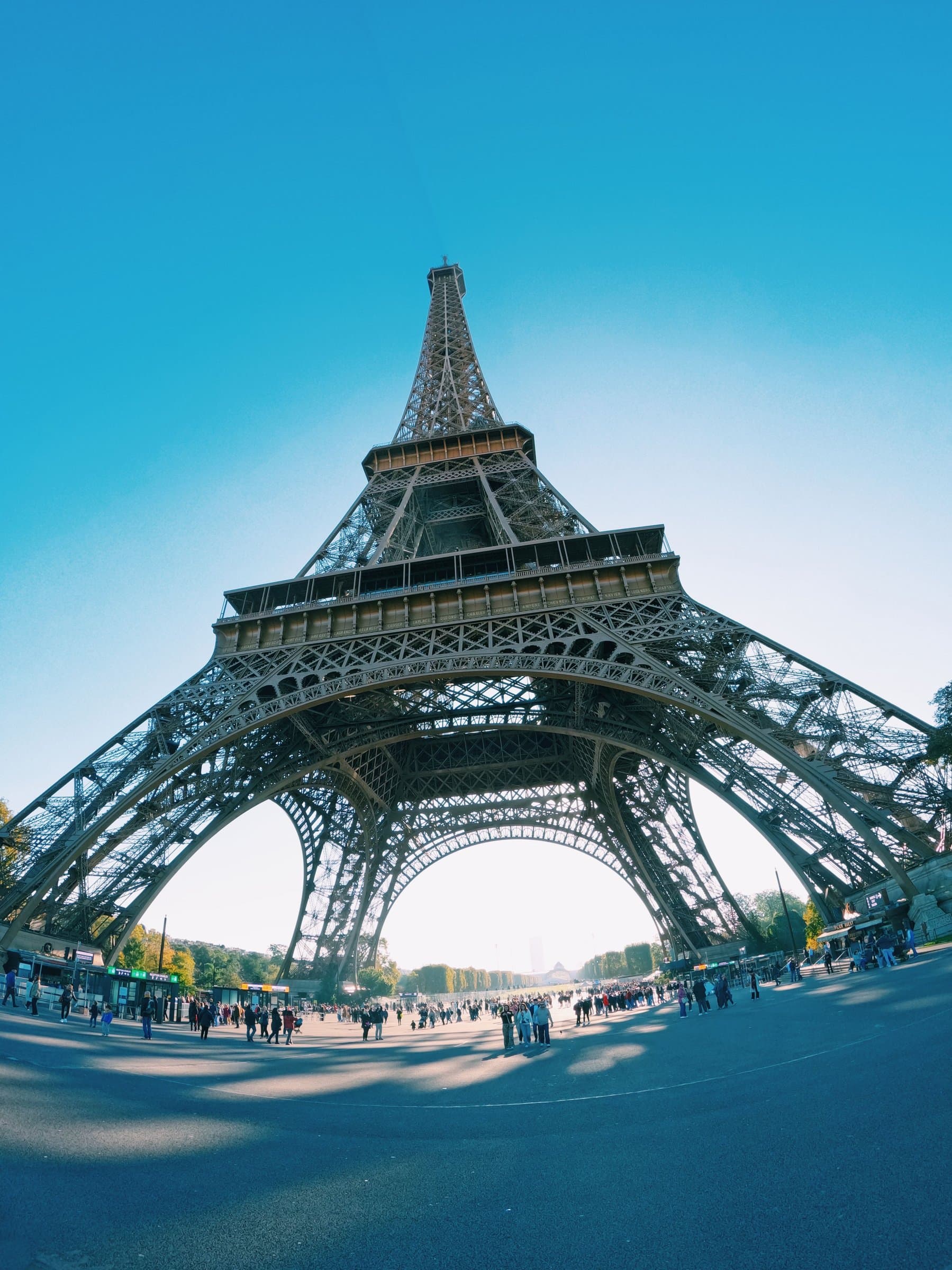 Looking up through the Eiffel Tower's iron arch from directly beneath it, crowds below.