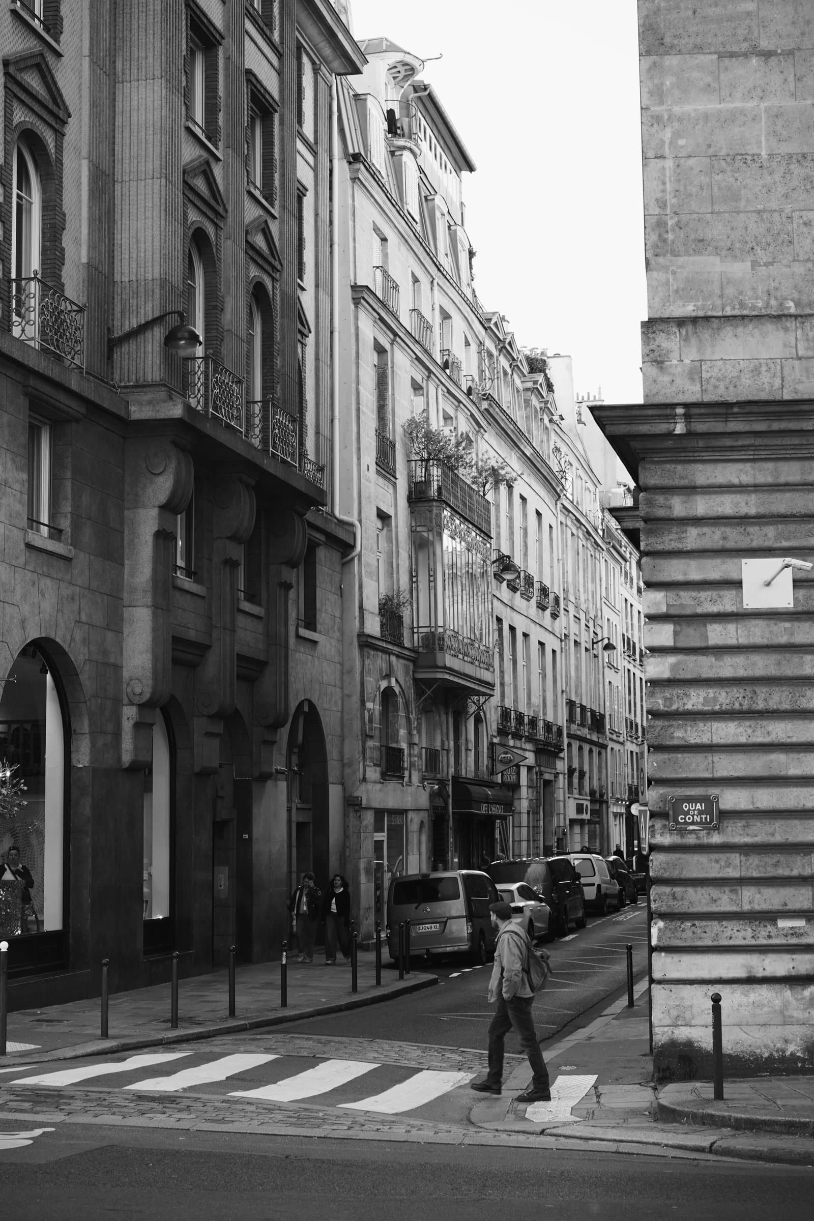 A black and white street scene of a Parisian corner, a man crossing at the zebra lines.