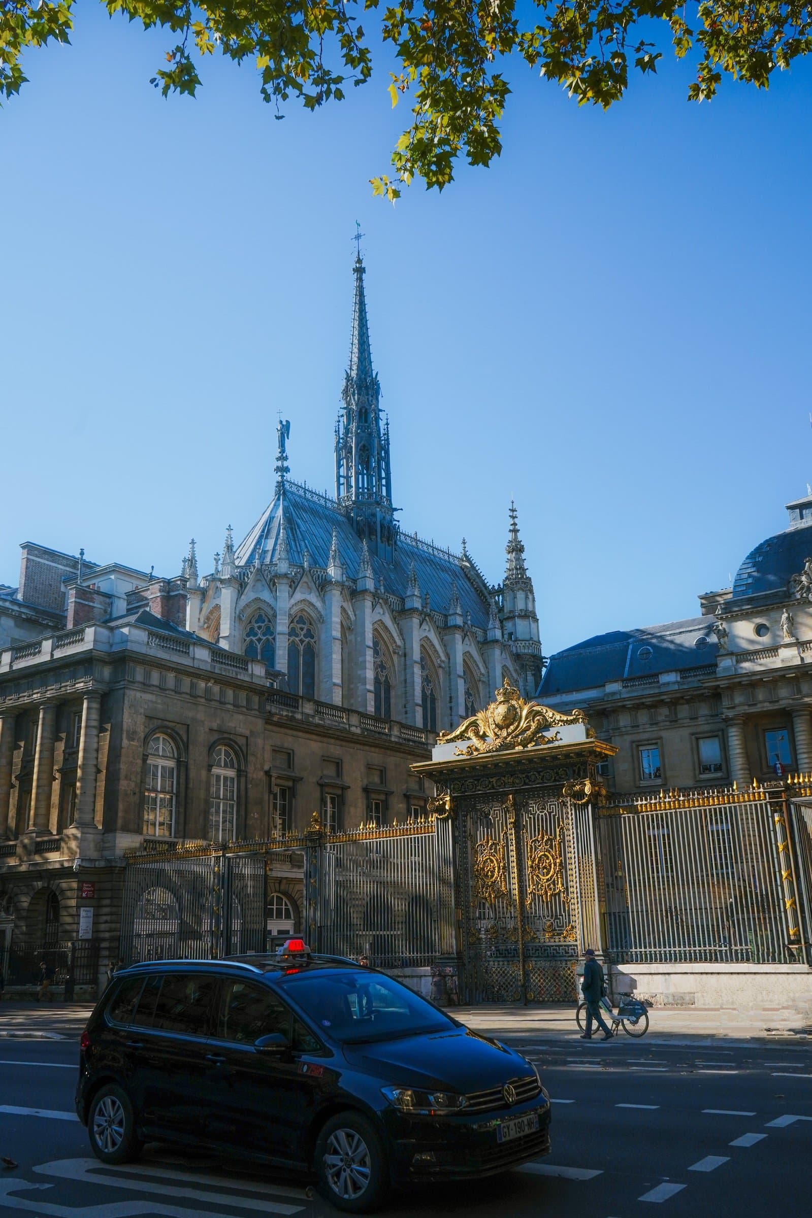 The Gothic spire of Sainte-Chapelle rises behind an ornate gilded gate under a clear sky.