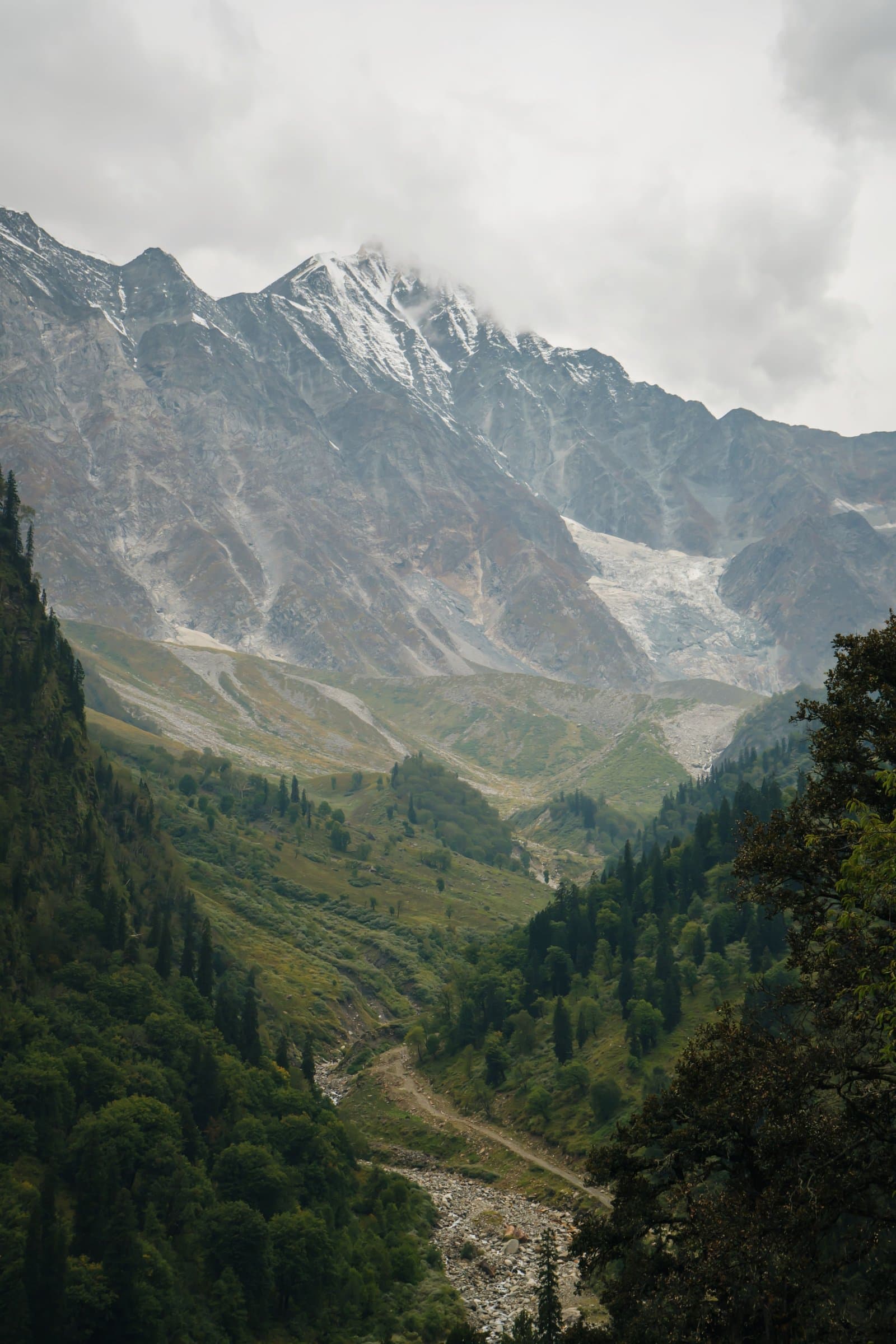 A misty green valley leads up to a glacier tucked between grey, snow-streaked peaks.