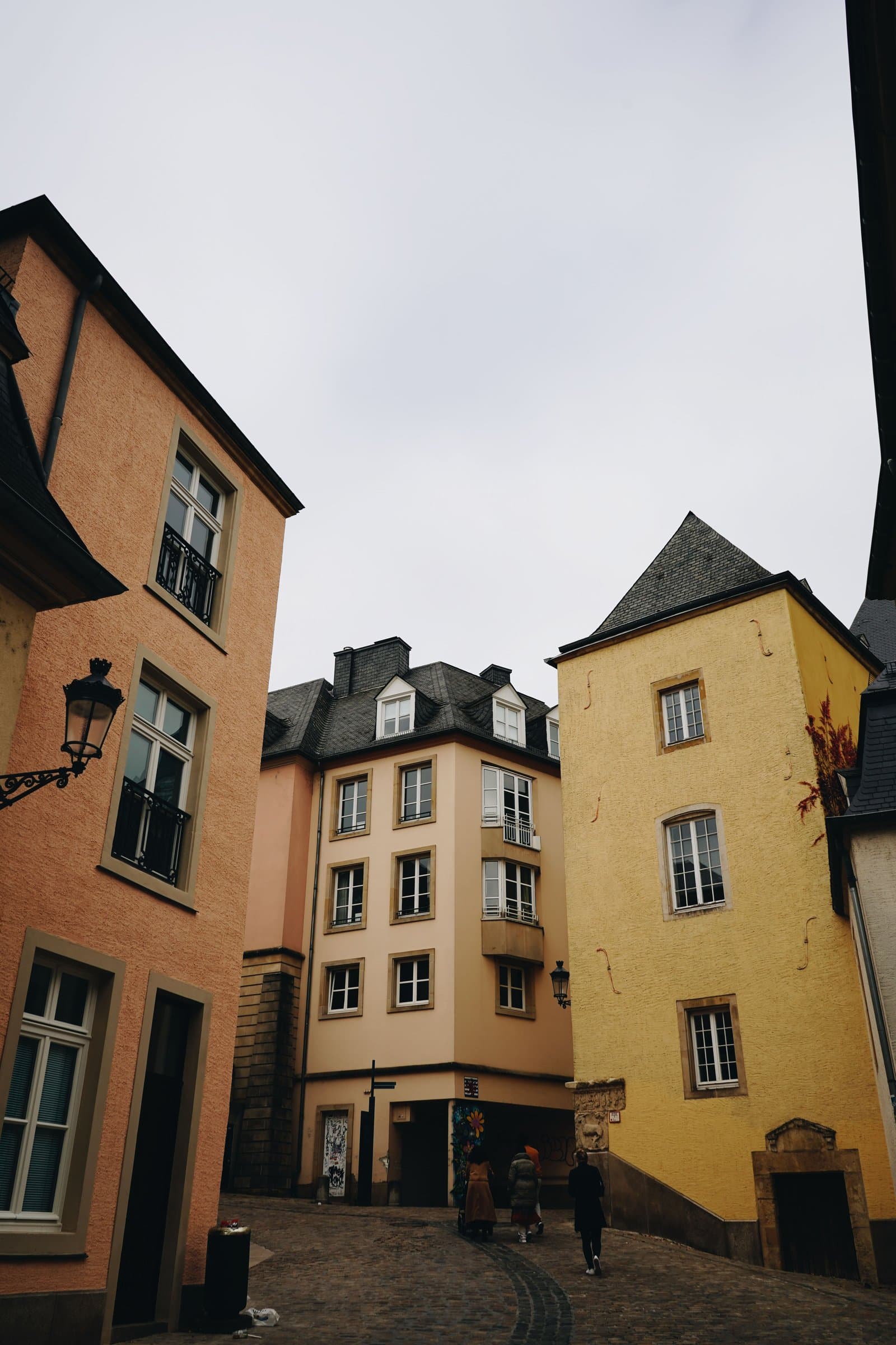 Peach, cream, and mustard-coloured old townhouses lean together above a cobbled square.